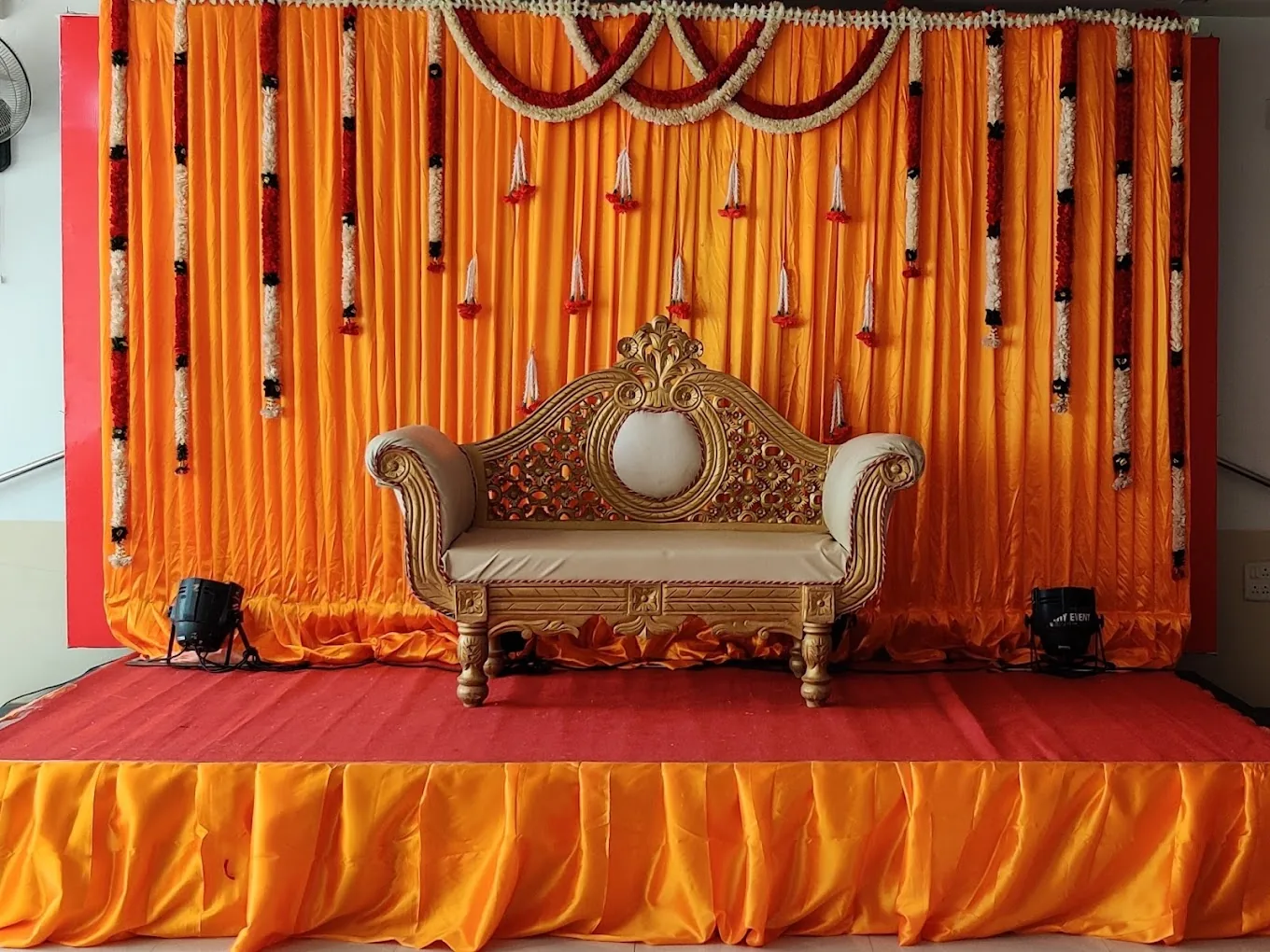 Saffron drapes and marigold strings behind a carved gold sofa