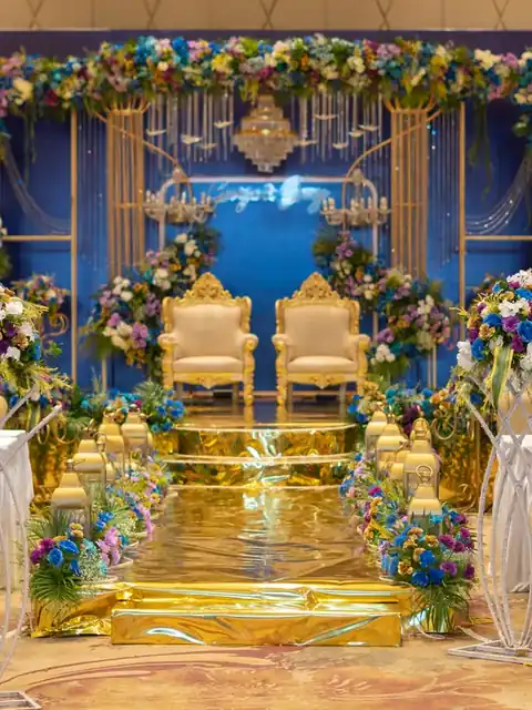 Reception stage in royal blue and gold, with carved gold chairs, floral arches and a gold mirrored aisle
